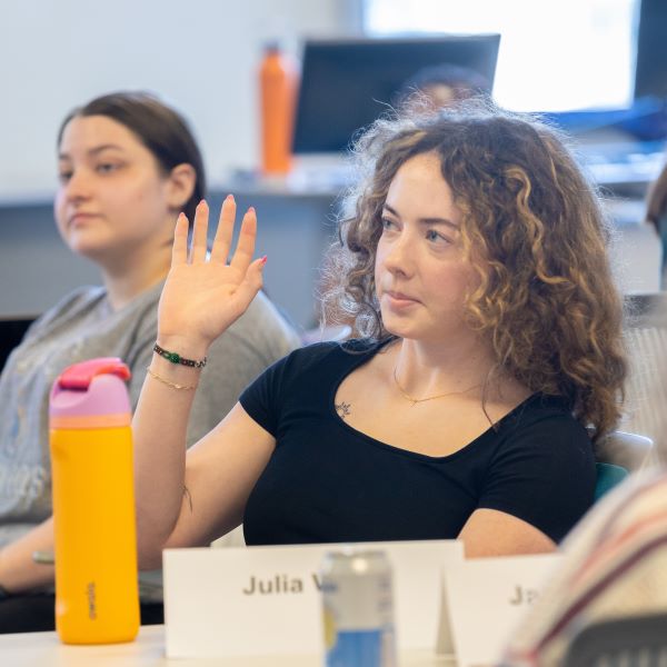 A student with curly hair looks interested in a seminar at the Bloch School. There are other students sitting at tables near her.