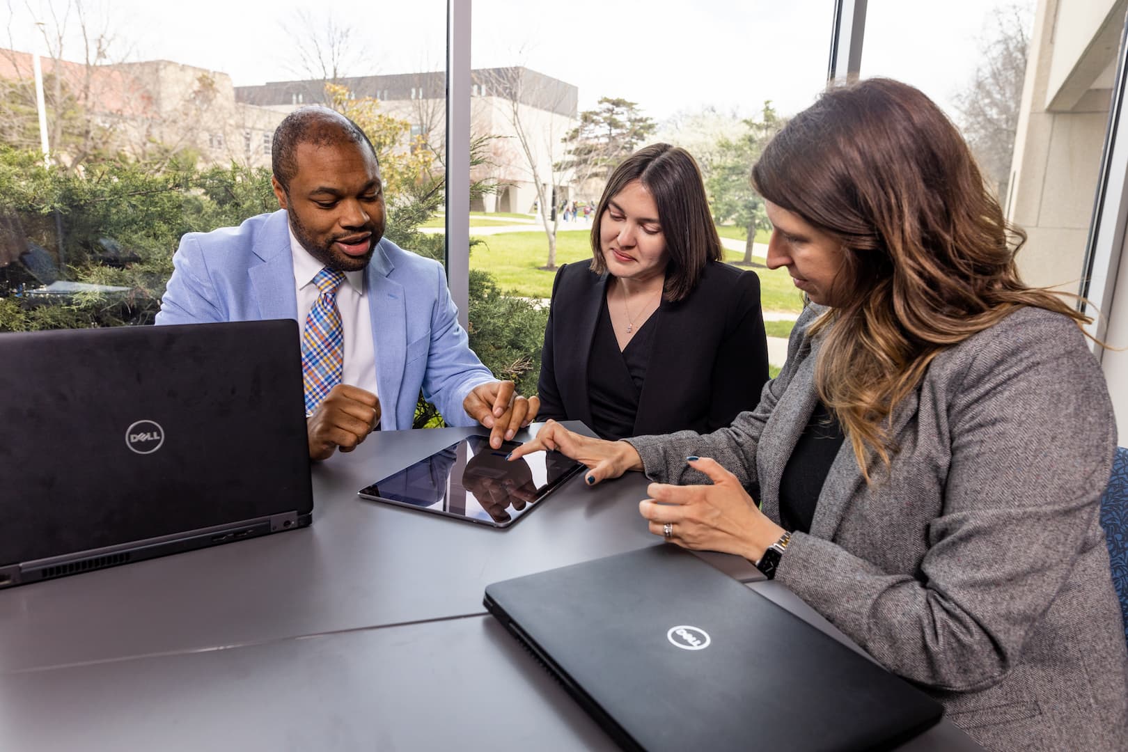 three staff members collaborate on a table while sitting at a table in front of windows in the UMKC Career Center