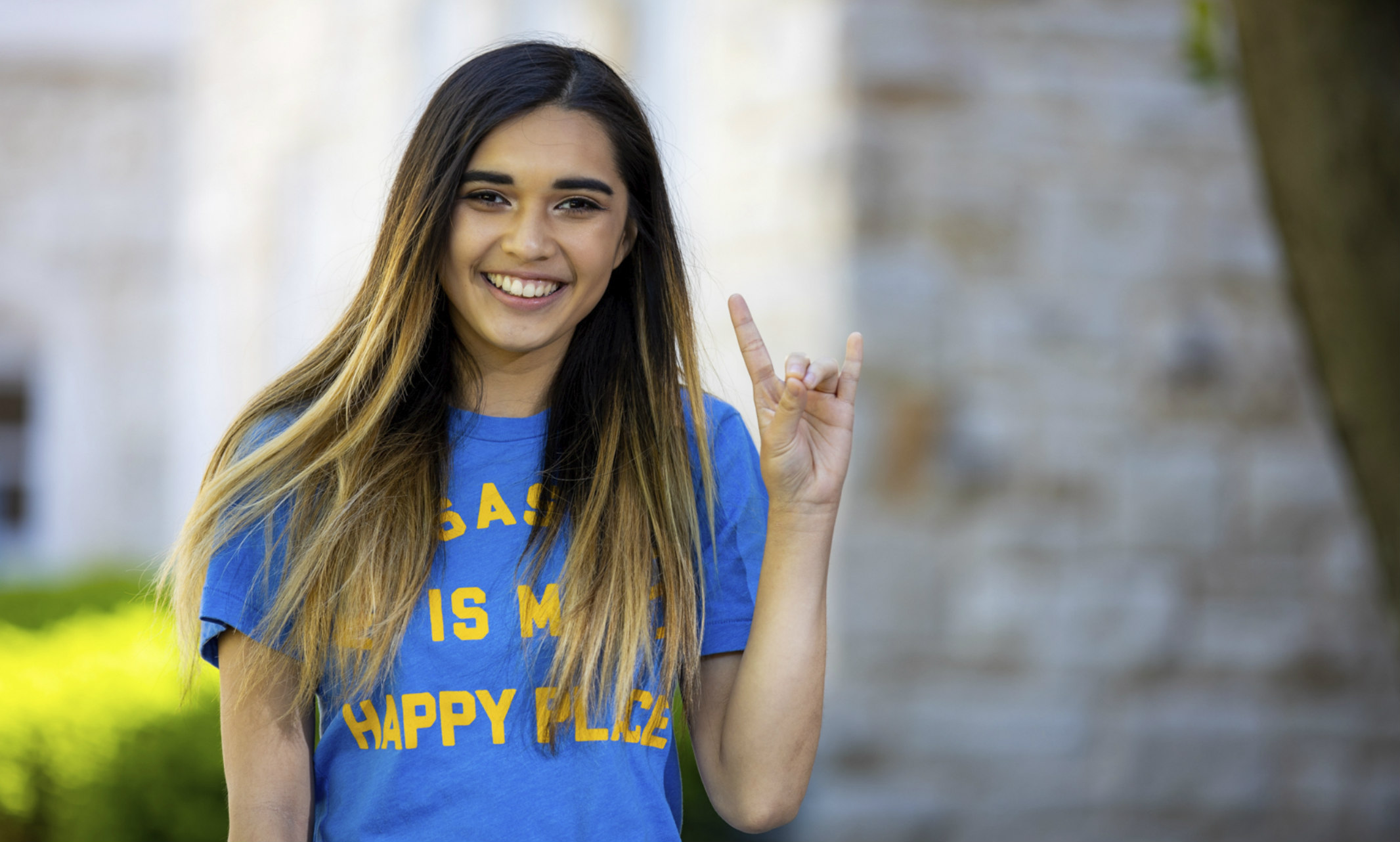 A student who presents as female wearing a blue T-shirt does the Roo sign with her hands.