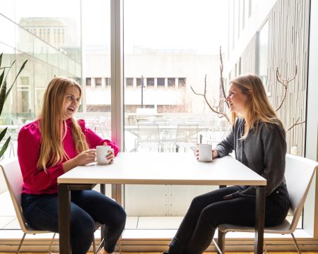 a student and a professor sit at a table and talk and drink coffee