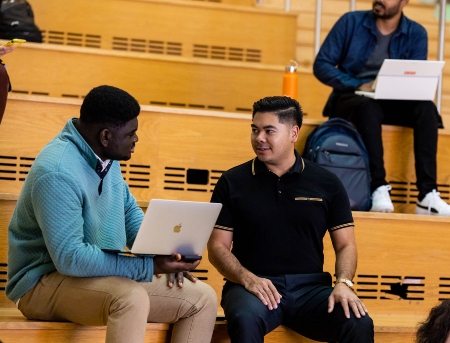 two students talk while sitting on bench at Bloch School