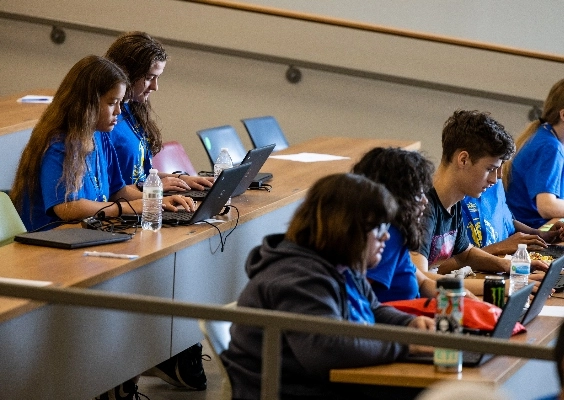 high school students take notes on laptops in lecture hall