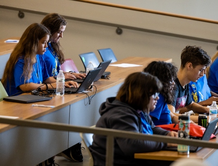 high school students take notes on laptops in lecture hall