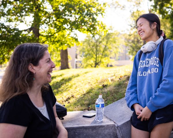 a professor speaks to a smiling student on the steps on campus