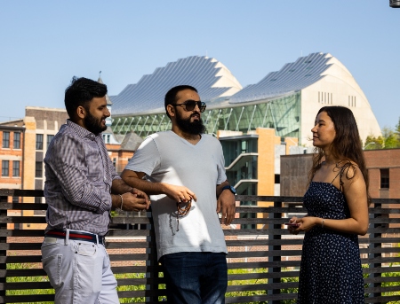 three students lean on a fence with the Kauffman Center in the skyline behind them