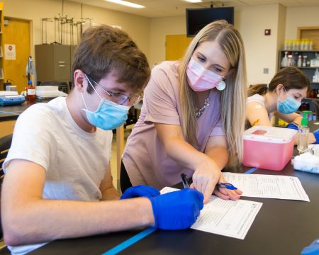 A graduate student holds open a book and looks at another student