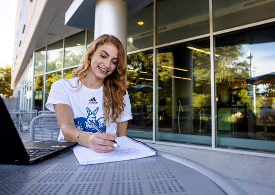 students sits outside student union with notebook and pen