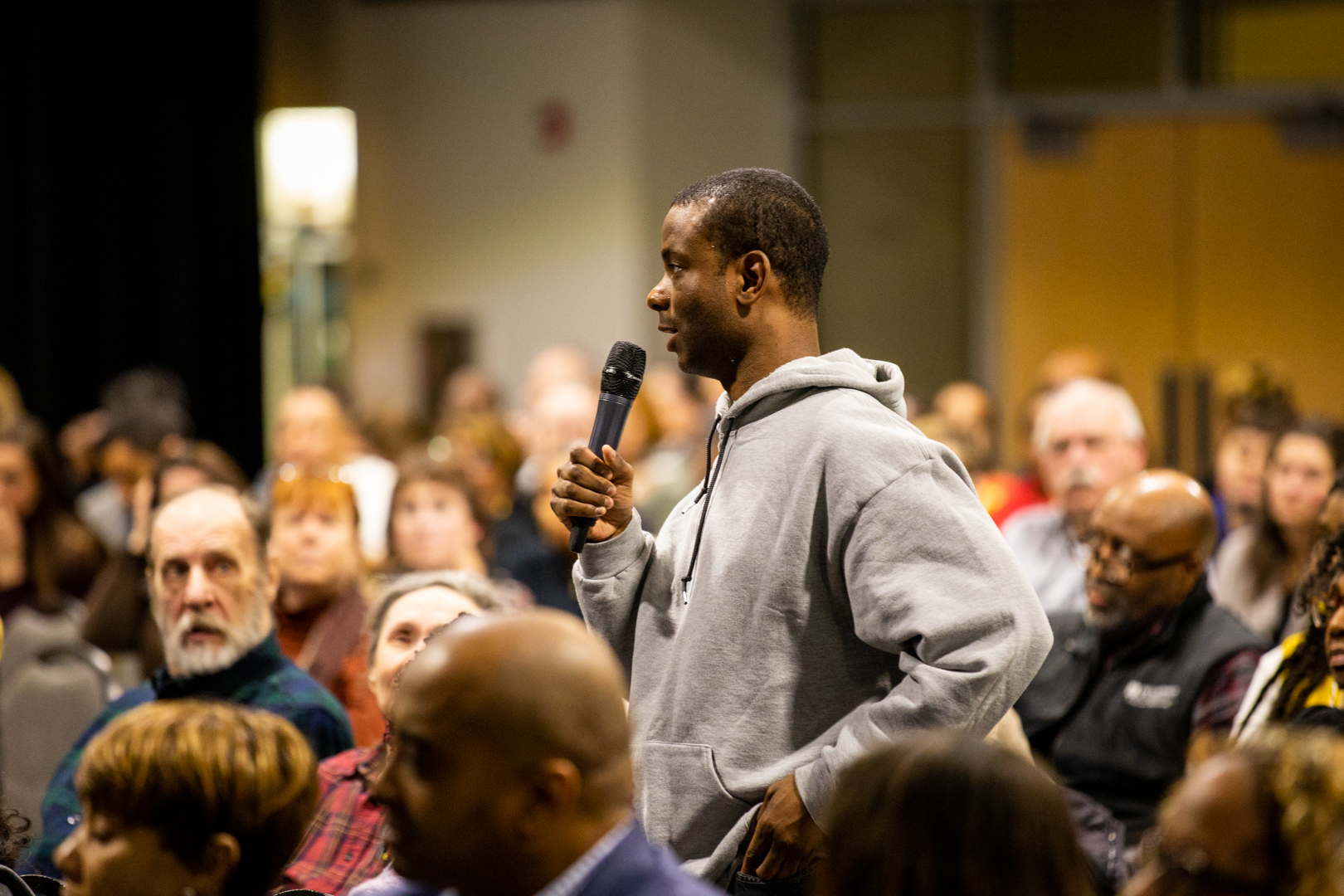 Audience member wearing a gray hoodie stands and asks a question during Harry Edwards lecture