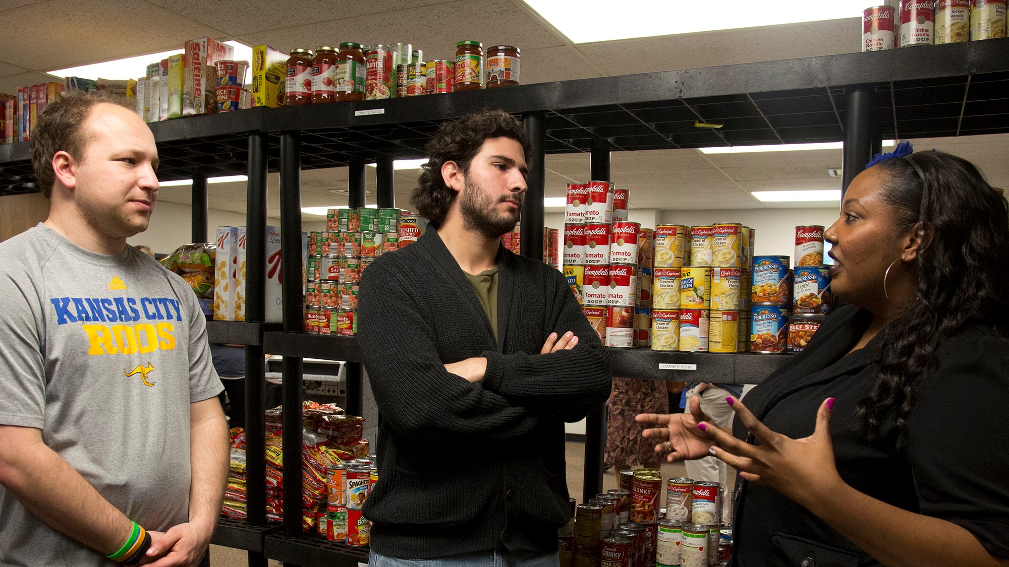 three staff members stand in front of shelves stocked with cans and boxes of food in the Kangaroo Pantry