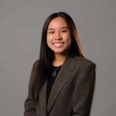 Smiling, Grace Yu, poses in a gray suit with a black shirt