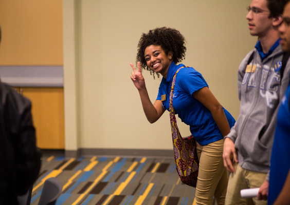 student wearing a blue UMKC polo shirt give the Roo Up hand sign at Orientation