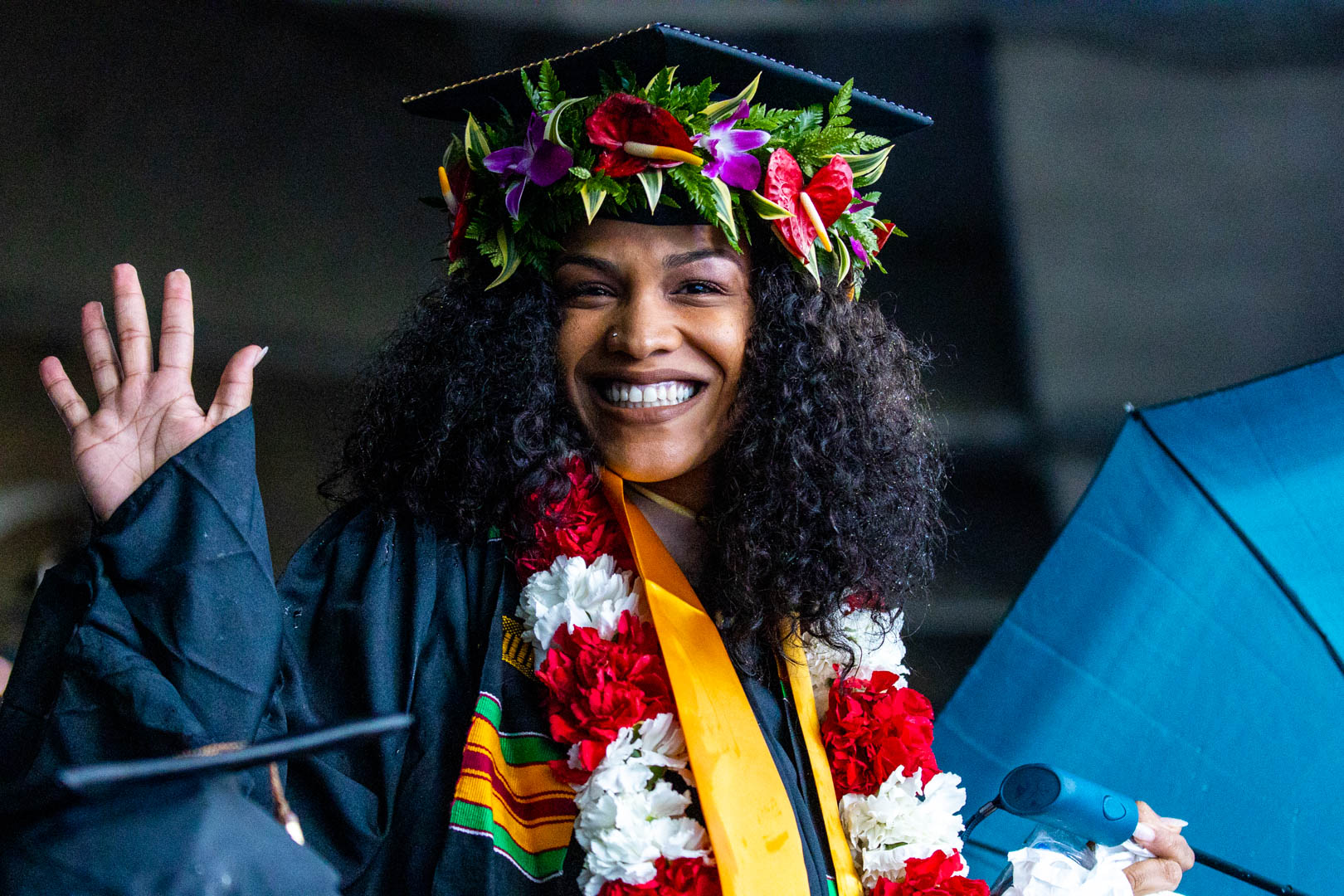 A graduate waves while wearing a flower wreath with her cap during commencement at Kauffman Stadium