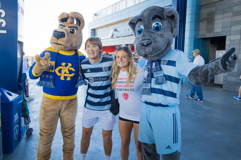 The UMKC mascot Kacey Roo, a fuzzy kangaroo, poses with two students and the Sporting KC mascot Blue the Dog