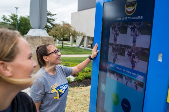 MCOM Students walking on campus and interacting with digital Kiosk