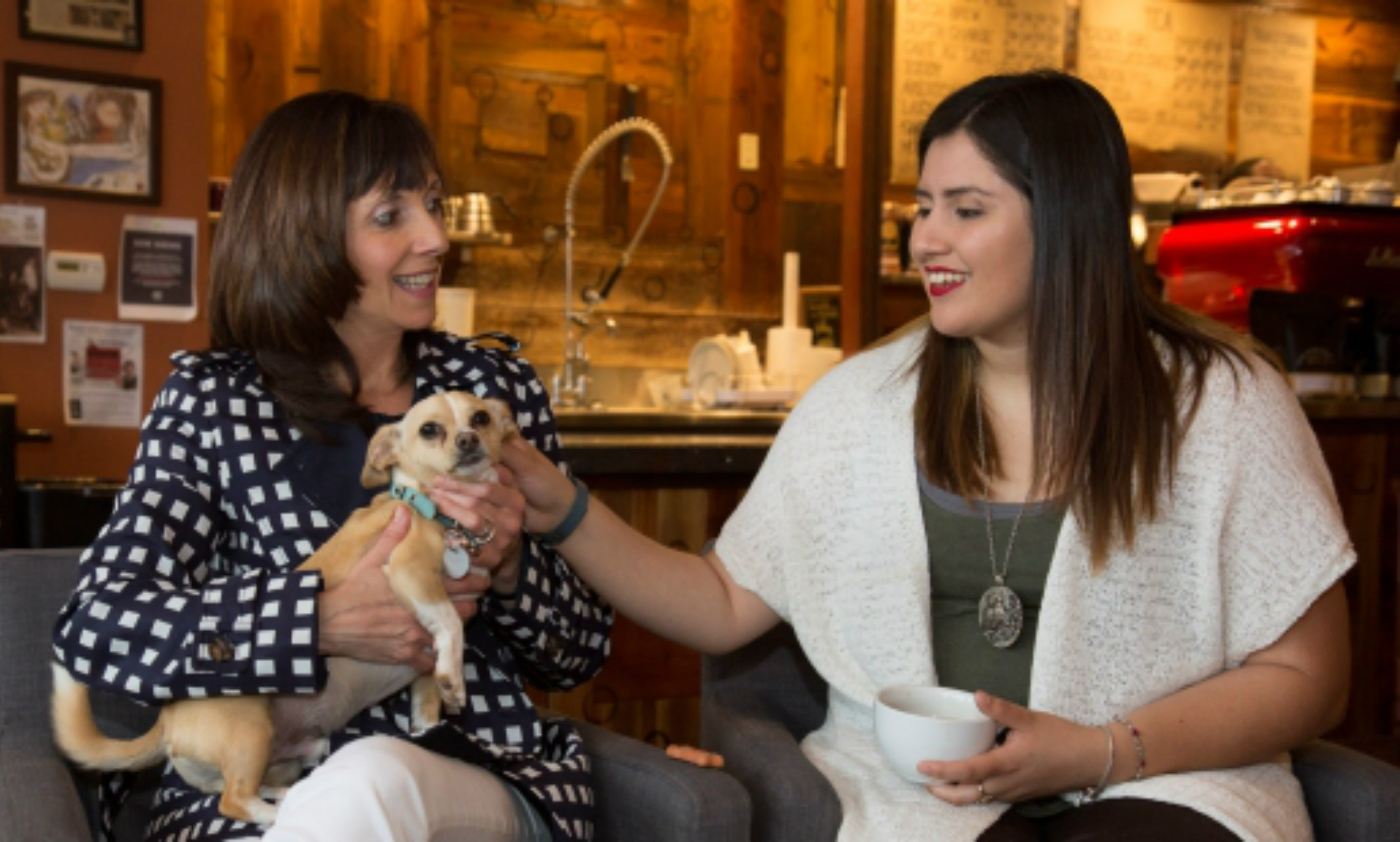 Two women sit in a coffee shop with a chihuahua.