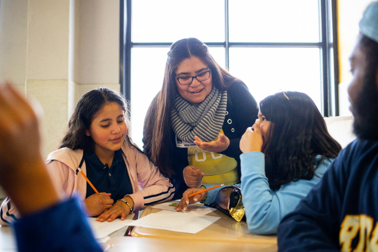 Astrid assists two female Hispanic students with worksheet activity