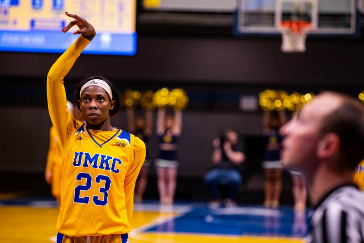A UMKC woman's basketball player stands with her arm in the air.