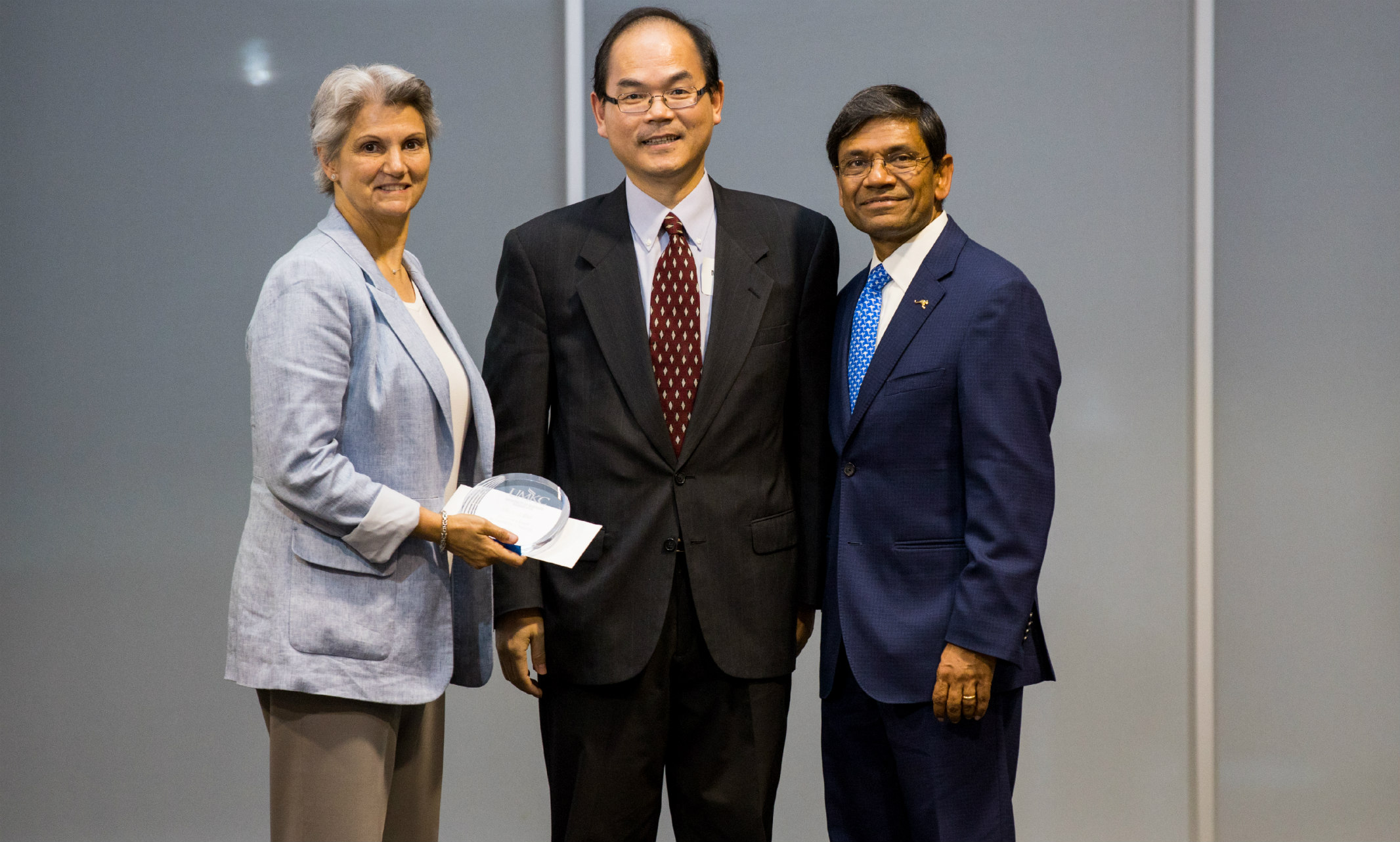 Michael Wei poses for photo holding award with chancellor and provost
