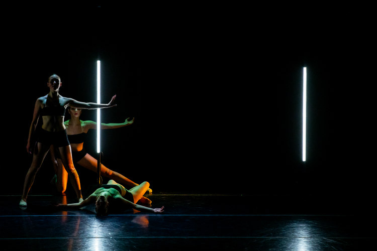 Three dancers are on a stage in a dark theater.
