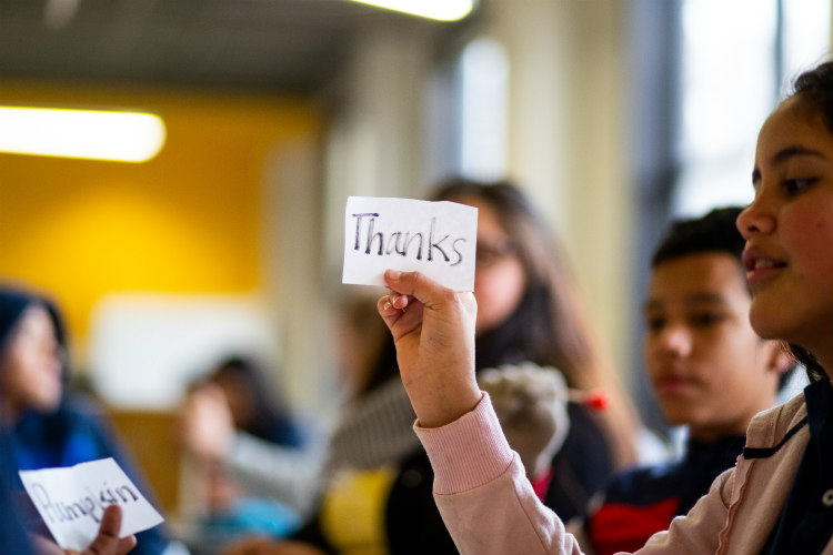 female Hispanic student holds up word card reading "thanks" during ELL group activity