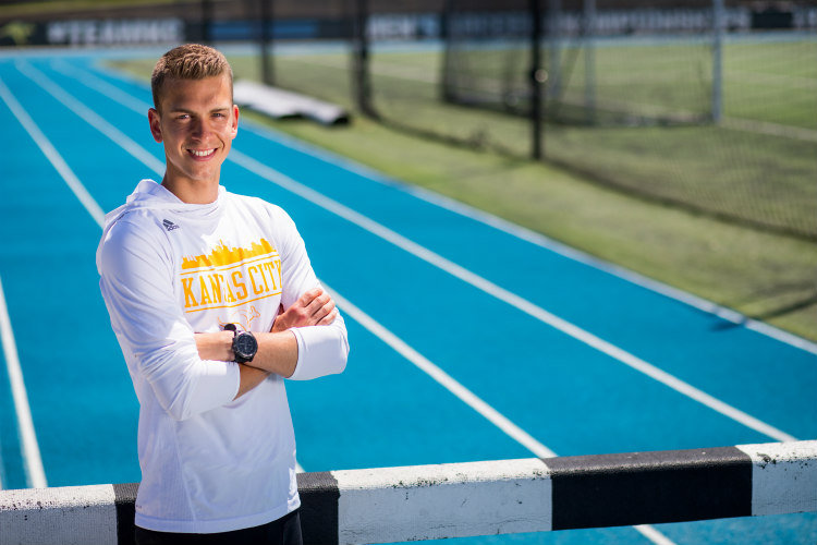 Bryce Miller standing with arms crossed in front of a hurdle on the track