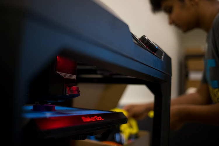 High school student focuses while hovered over working with 3D printing macine