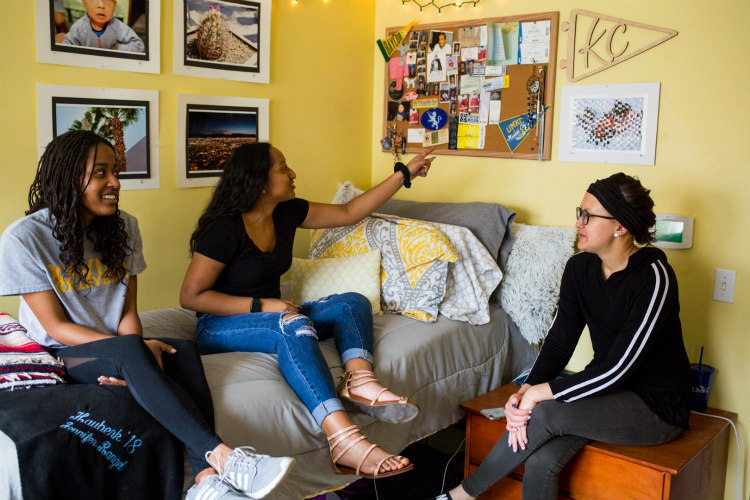 Three women are sitting in a dorm talking.