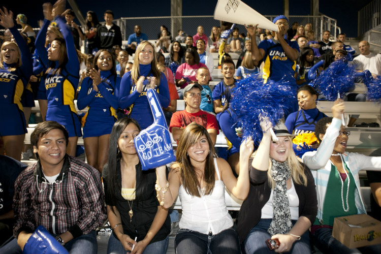 A group of diverse students sitting on outdoor bleachers; one is holding a UMKC finger sign