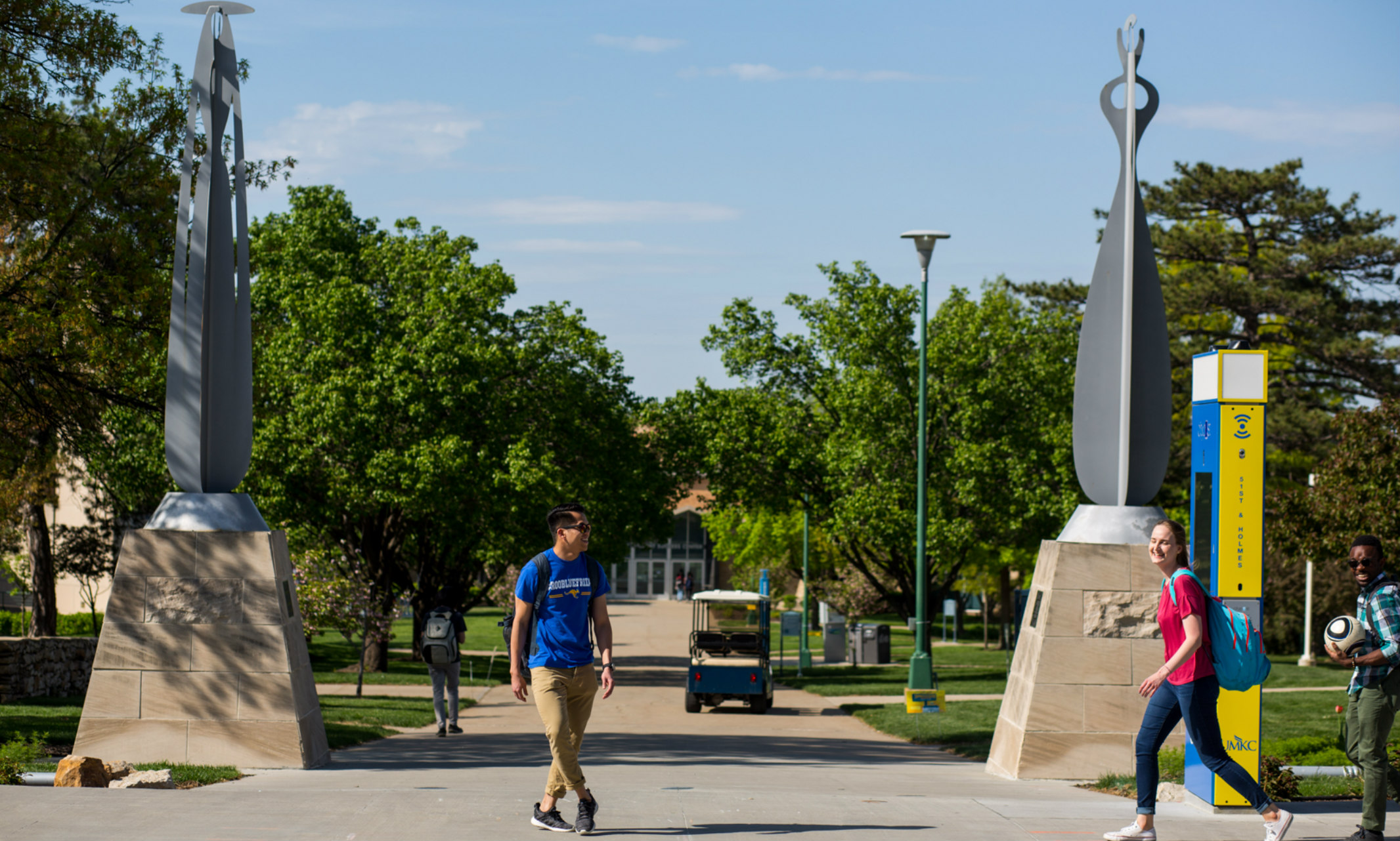 Several diverse students walking on UMKC campus near the pair of Archipenko sculptures