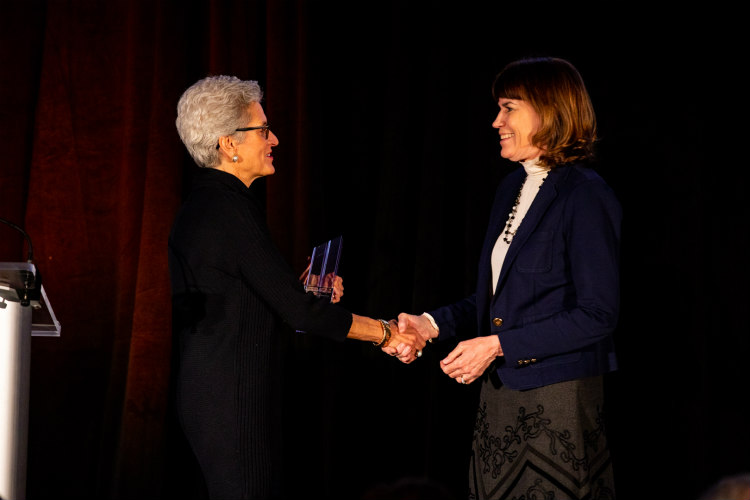 Meyers accepts award from Mary Bloch as they shake hands on stage