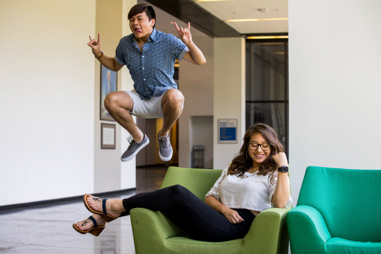 A student leaps in the air while another sits in a green chair.