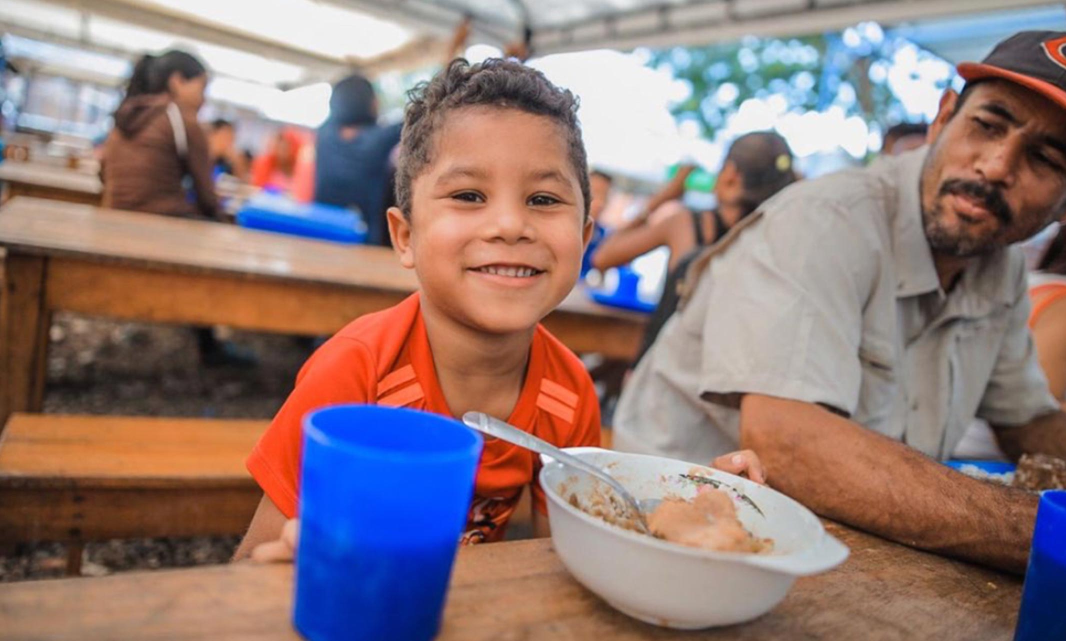 Venezuelan boy and his father eating a meal at a refugee aid center in Colombia