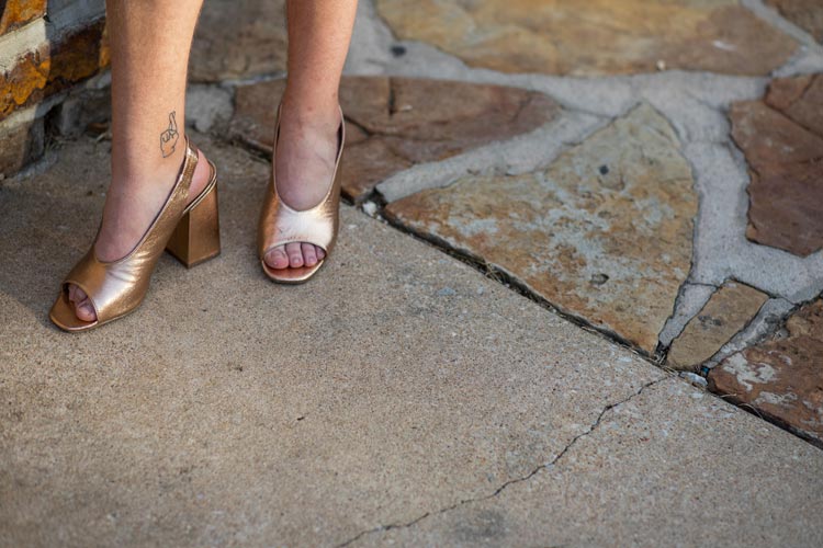 close-up of a man's feet in heels, can see a fingers-crossed tattoo on the ankle