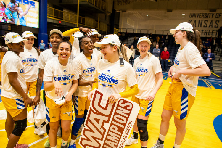 Ericka holds WAC championship sign smiles while interacting and celebrating with teammates