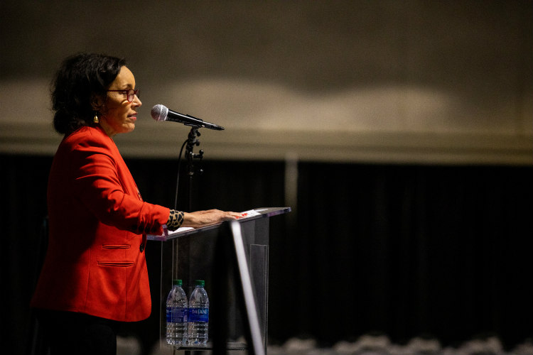 Susan Wilson speaking at podium wearing red jacket