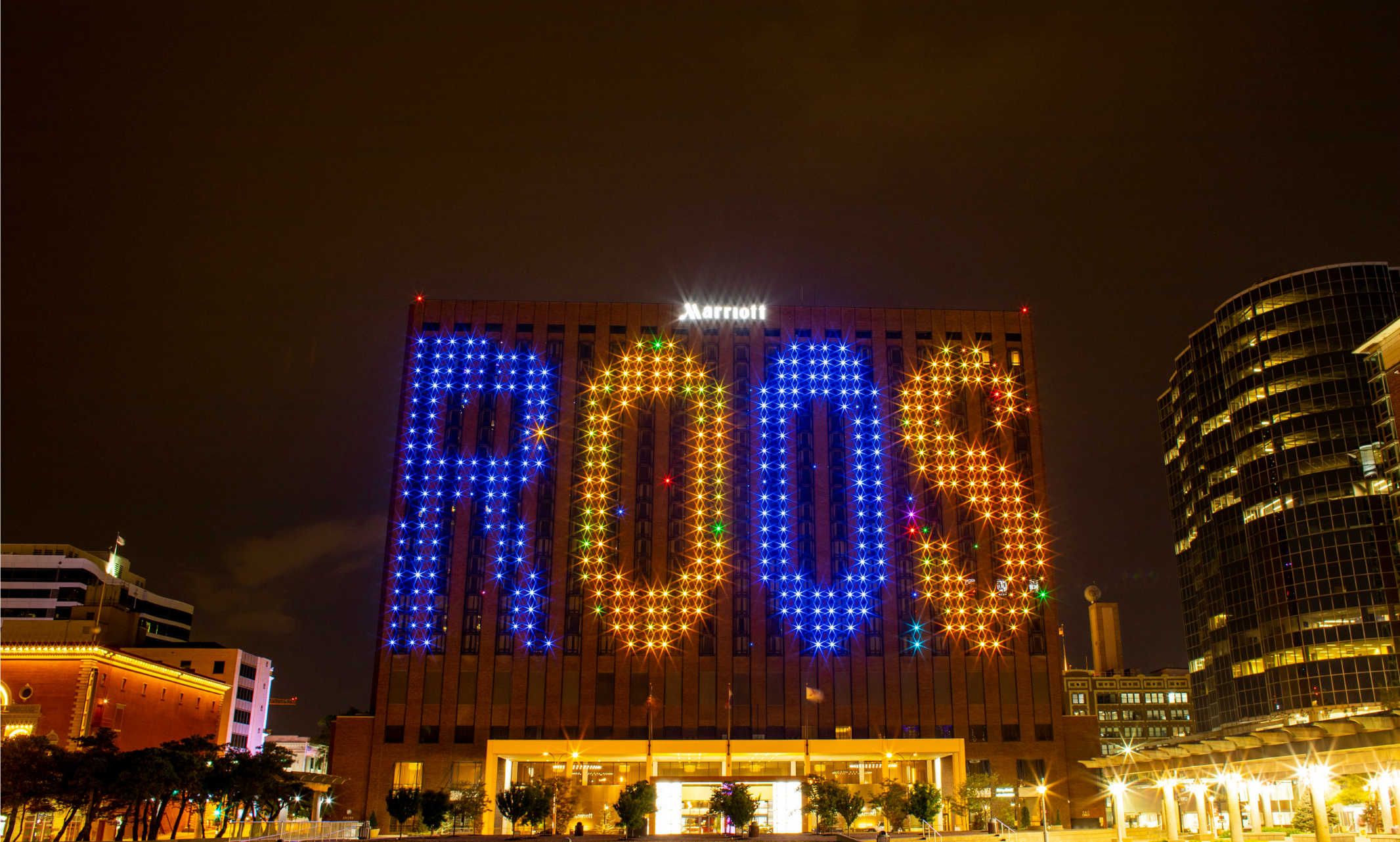 Photo of Marriott Holtel in downtown Kansas City lit up blue and gold with ROOS on the outside of the building