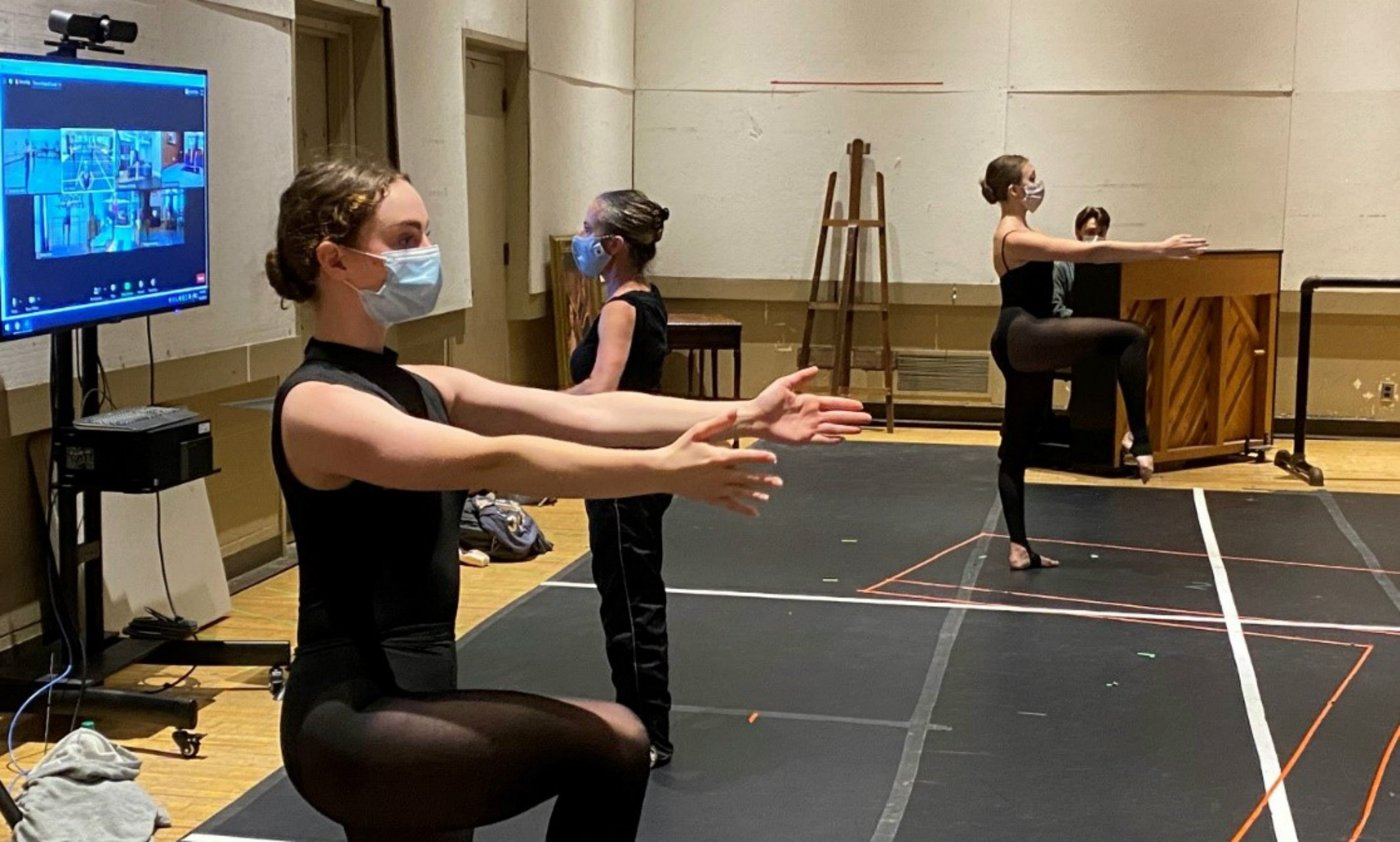 dancers with masks practicing while instructor with mask checks on students on Zoom