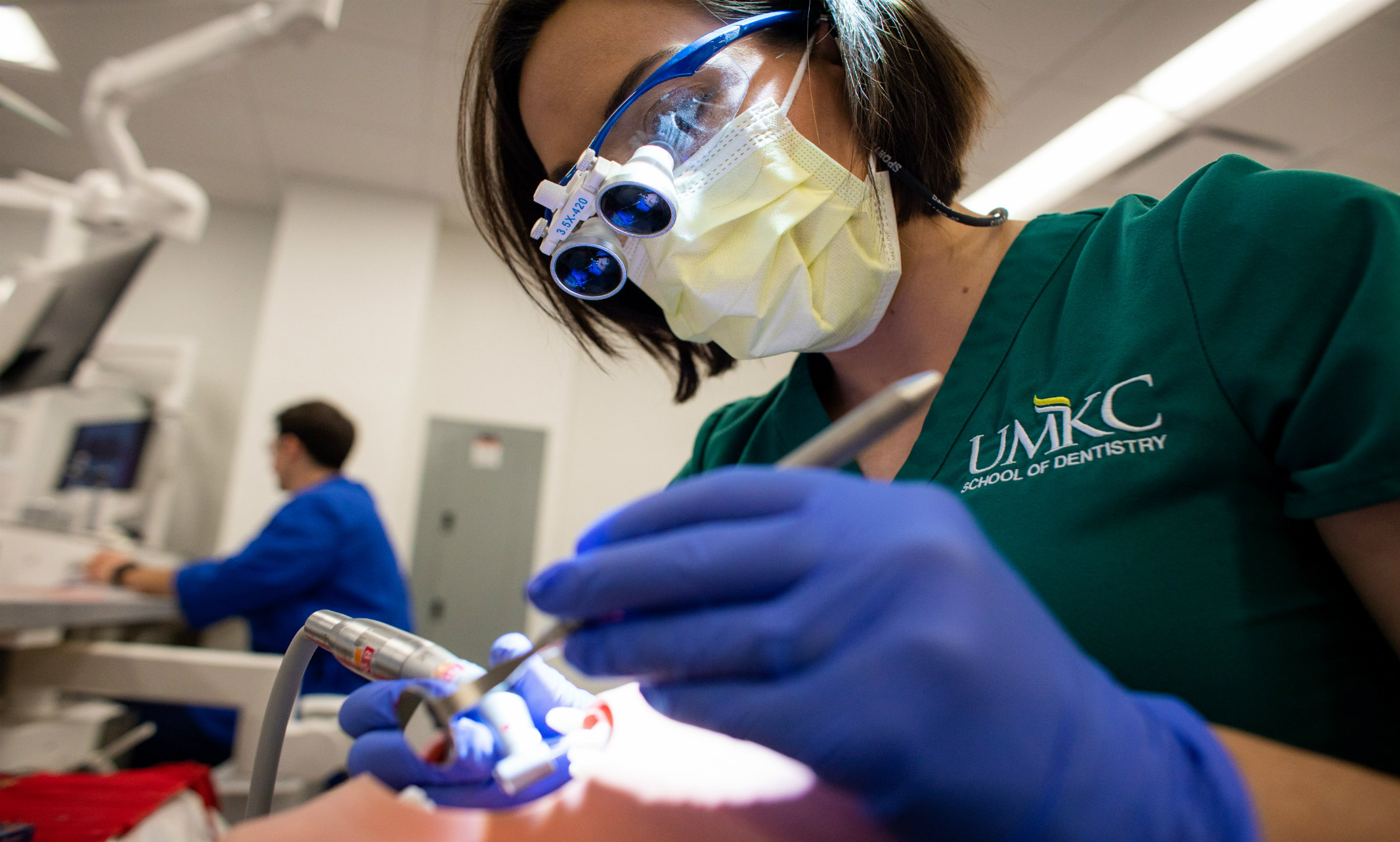 Student wearing mask performing over a mannequin in UMKC School of Dentistry simulation lab