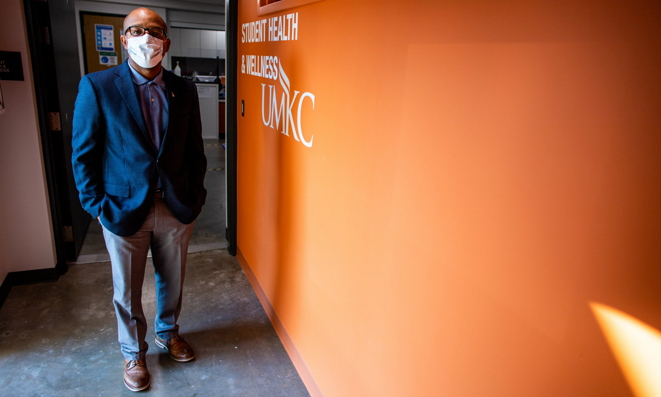 Obie Austin standing near orange student health wall wearing mask