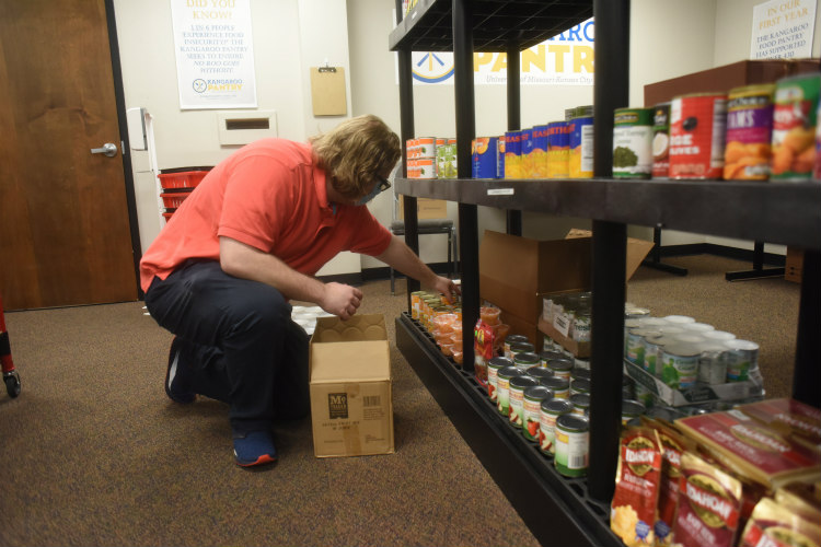 Sam Weis, graduate assistant at the pantry stocks shelves with new food arrivals.