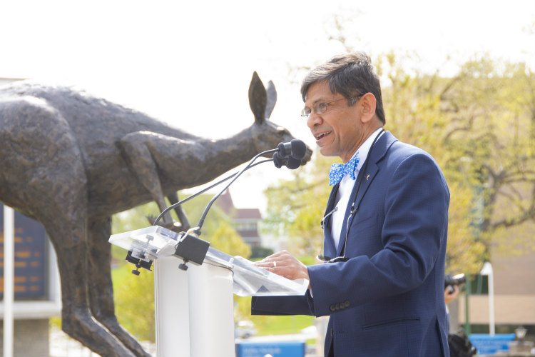 Chancellor Agrawal speaks into a microphone with the bronze Roo sculpture looming in background