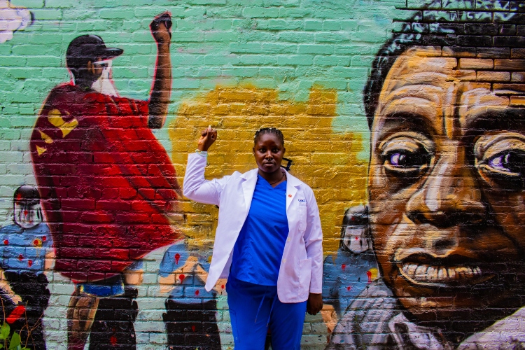 Coco Ndipagbor stands in front of a mural with a fist held in the air
