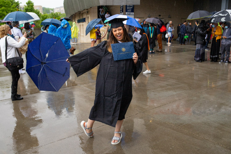 Female in regalia with diploma and umbrella in the rain