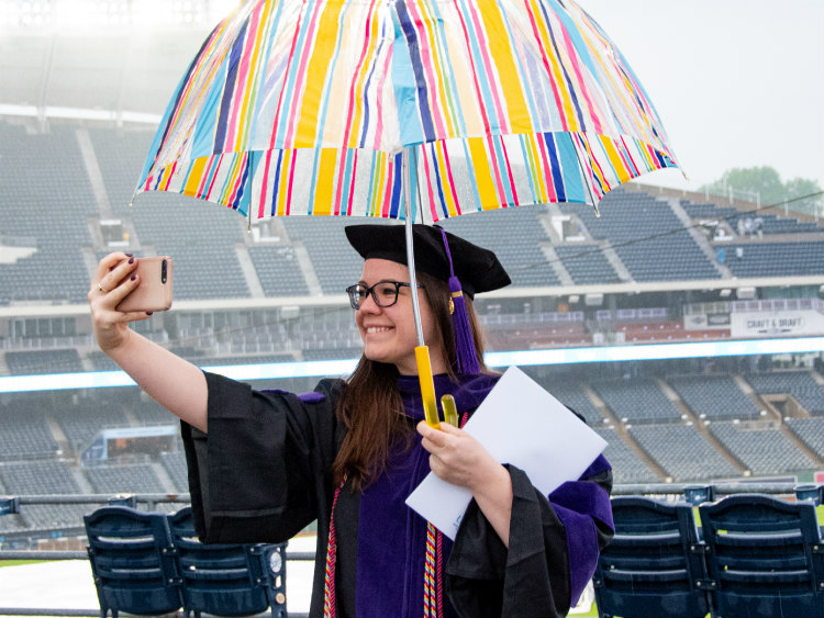 Female student with stadium in background holding an umbrella