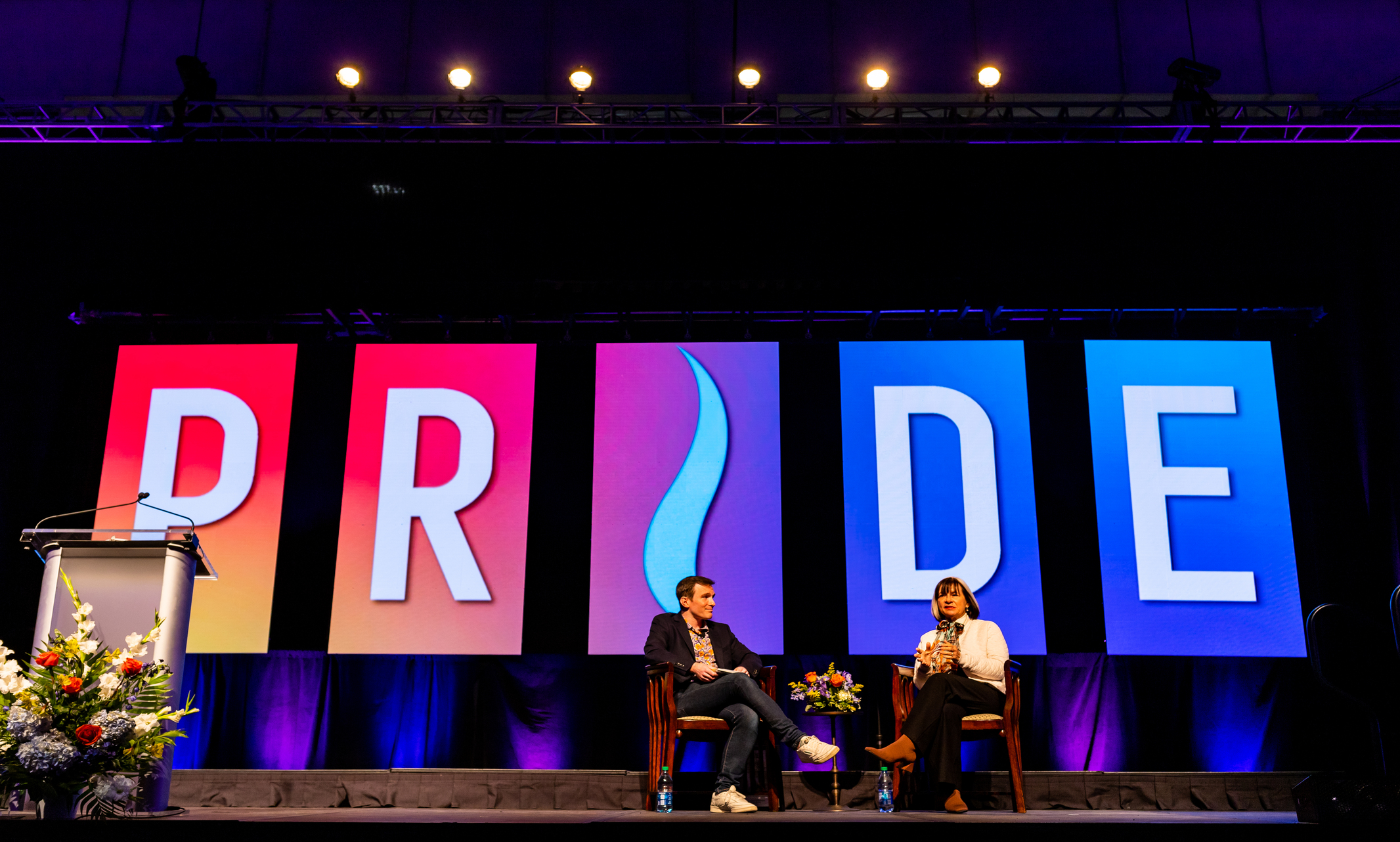 Two people sit on stage at the Pride Breakfast