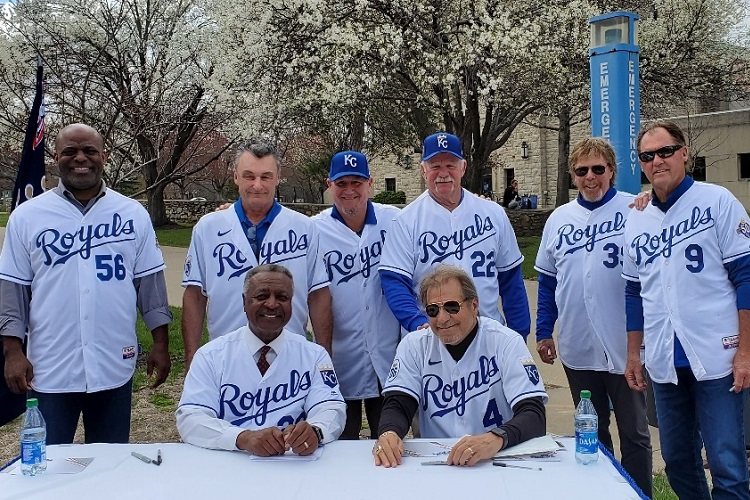 Eight former Royals players stand together and smile at the camera. All are wearing jerseys with their former numbers.