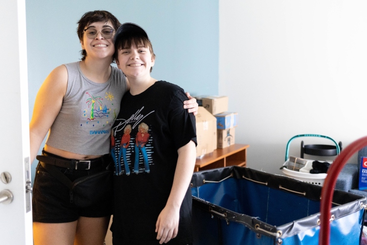 Roommates stand in their room smiling as they unpack at the Hospital Hill Apartments