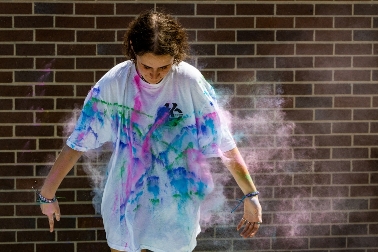 A student stands in a white shirt with color powder flying toward her, dying her shirt.