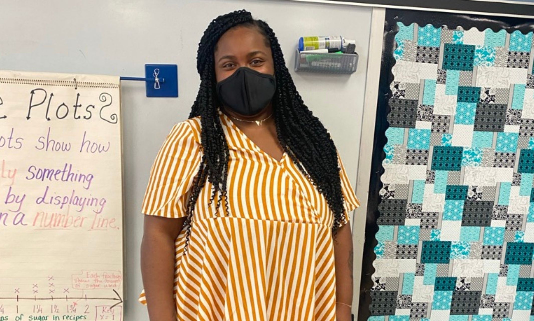 Xai Brooks wears a mask and stands in the front of her classroom
