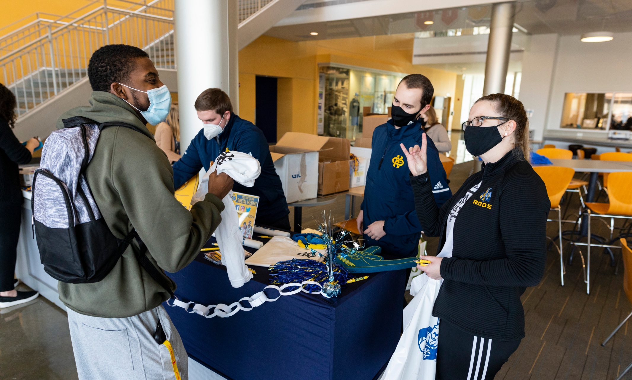 students in masks talk around a table with UMKC giveaway items
